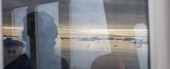 Bootsfahrt durch die Diskobucht mit Blick durch das Bootsfenster, Spiegelung von Bergen und Personen während einer Fotoreise nach Grönland