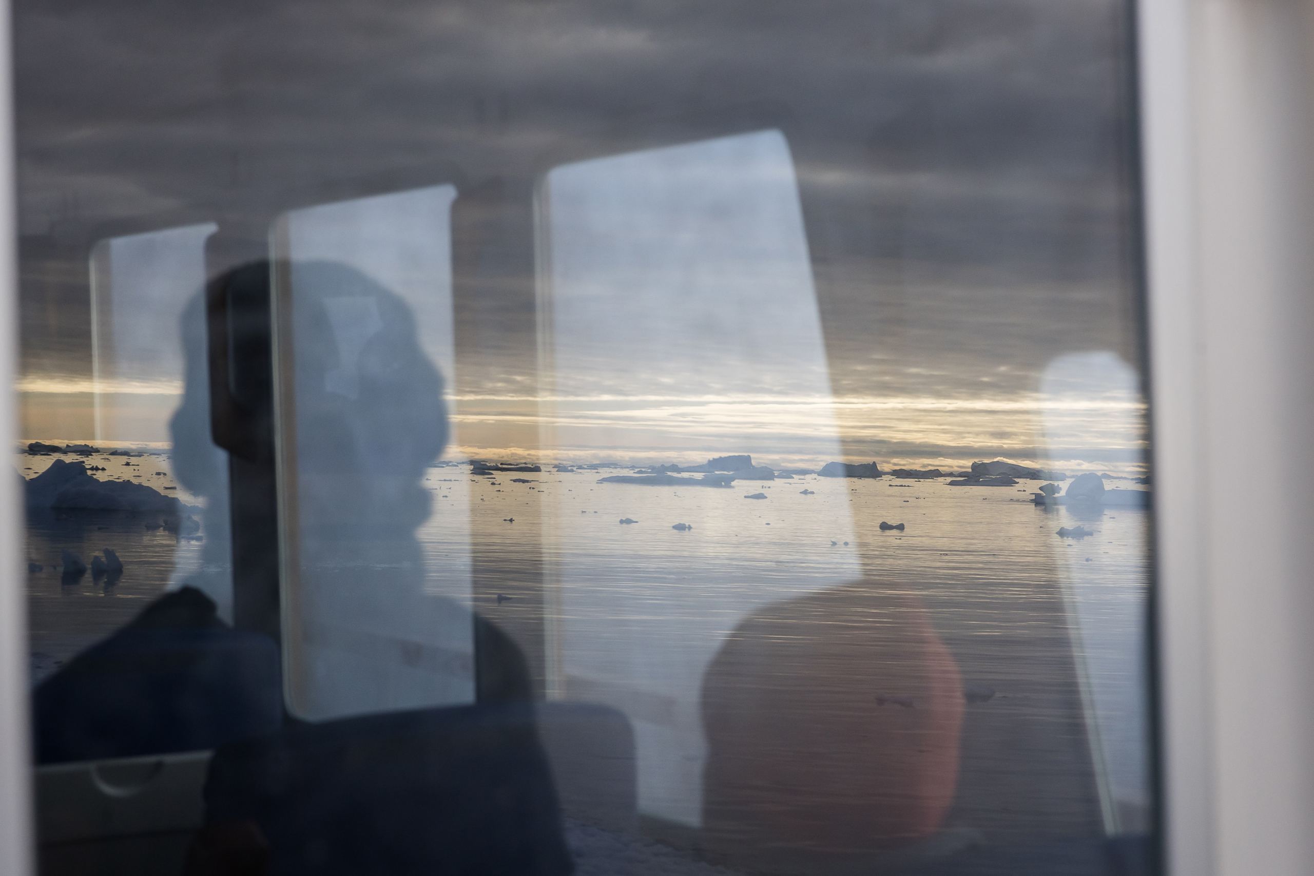 Bootsfahrt durch die Diskobucht mit Blick durch das Bootsfenster, Spiegelung von Bergen und Personen während einer Fotoreise nach Grönland