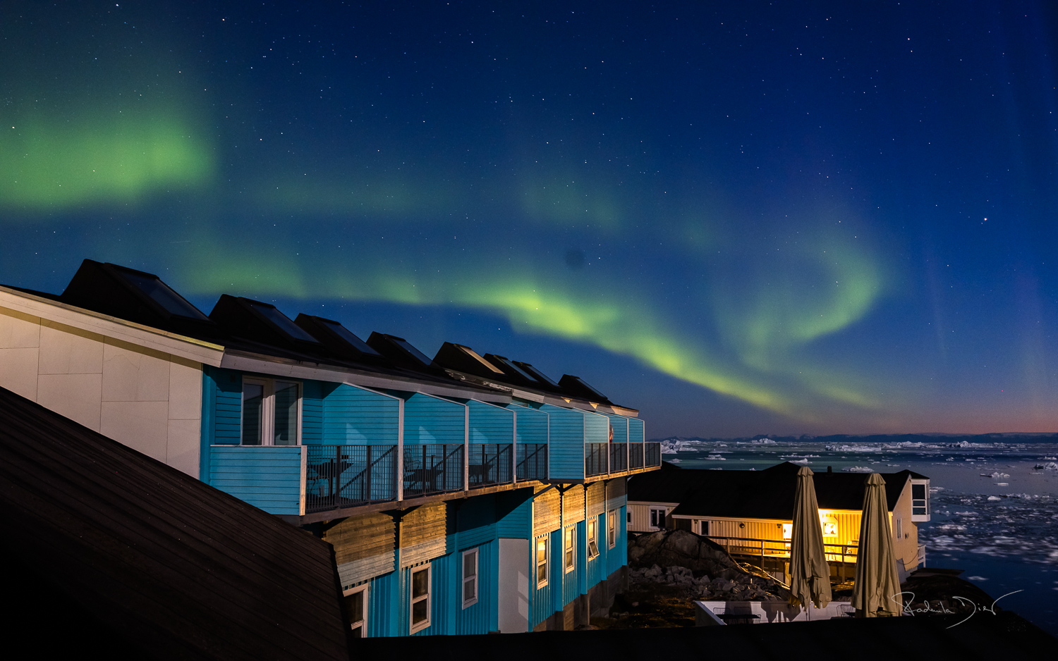 Polarlichter über Ilulissat – Nordlicht über der Diskobucht Hands on Camera Nordlichter über Ilulissat, fotografiert vom Hotelzimmerbalkon mit Blick auf die Diskobucht und die arktische Landschaft.