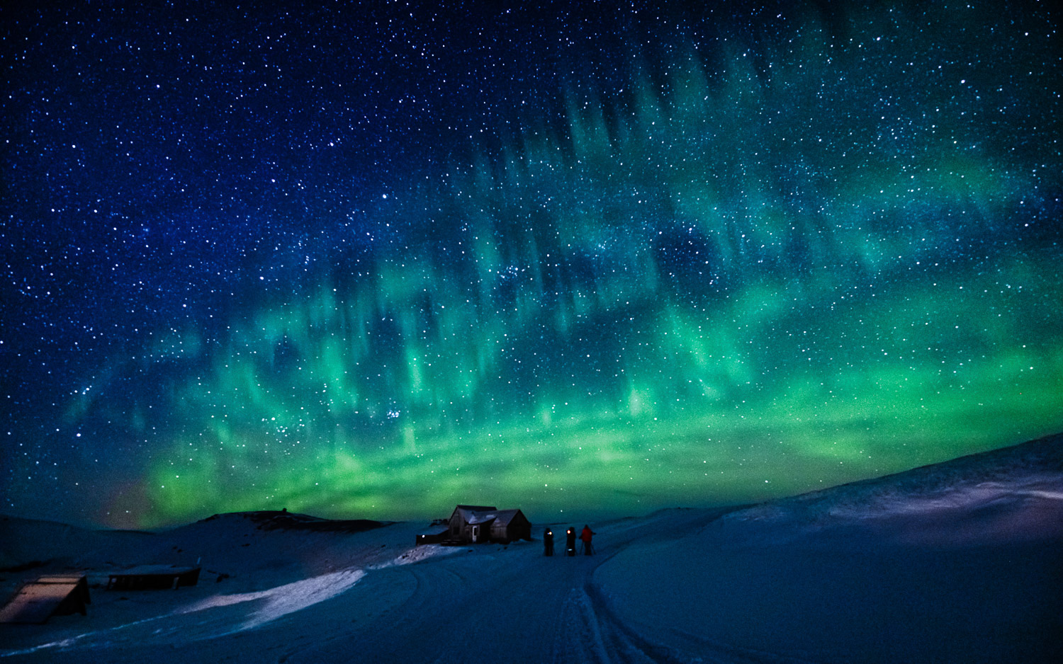 Polarlichter bei der Highland Base in Kerlingarfjöll Grüne Polarlichter am Sternenhimmel über verschneiten Hütten und Menschen in Kerlingarfjöll, direkt vor der Highland Base.