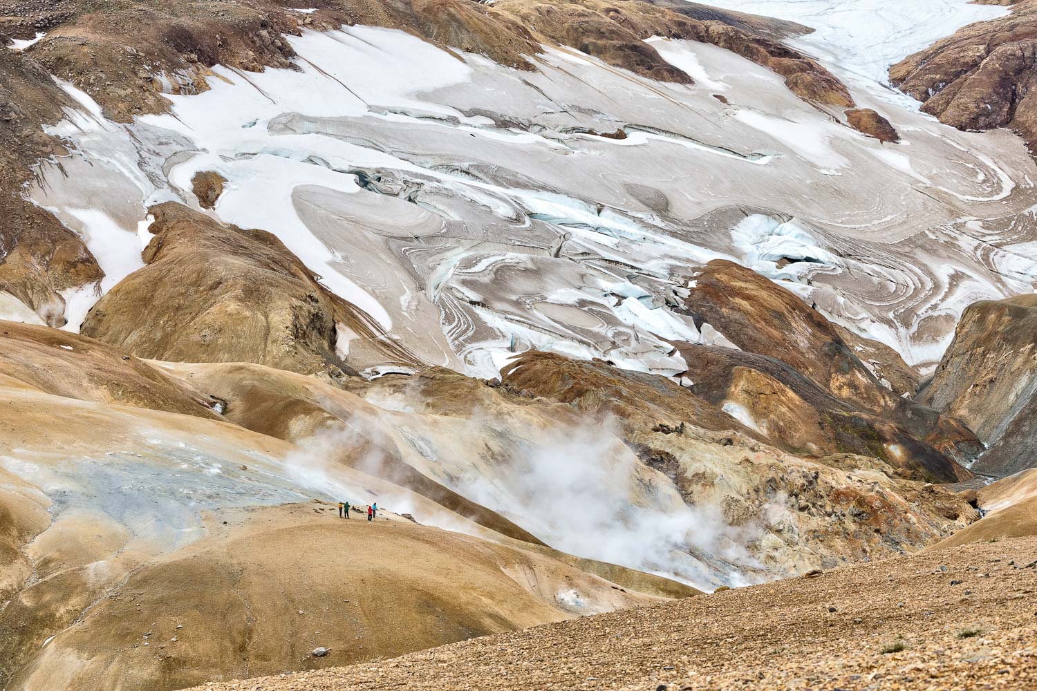 Kerlingarfjöll – Fotoreise Island Nord & Hochland Ockerfarbene Berge, Schneefelder und aufsteigender Dampf in Hveradalir im isländischen Hochland, mit Wanderern im Vordergrund.