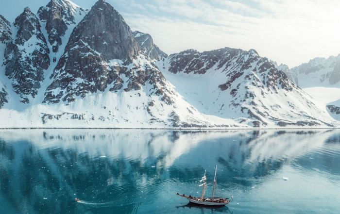 Segelschiff Ocean Sherpa im Scoresbysund in Ostgrönland – Spiegelung der schneebedeckten Berge im türkisblauen Wasser unter klarem arktischem Licht.