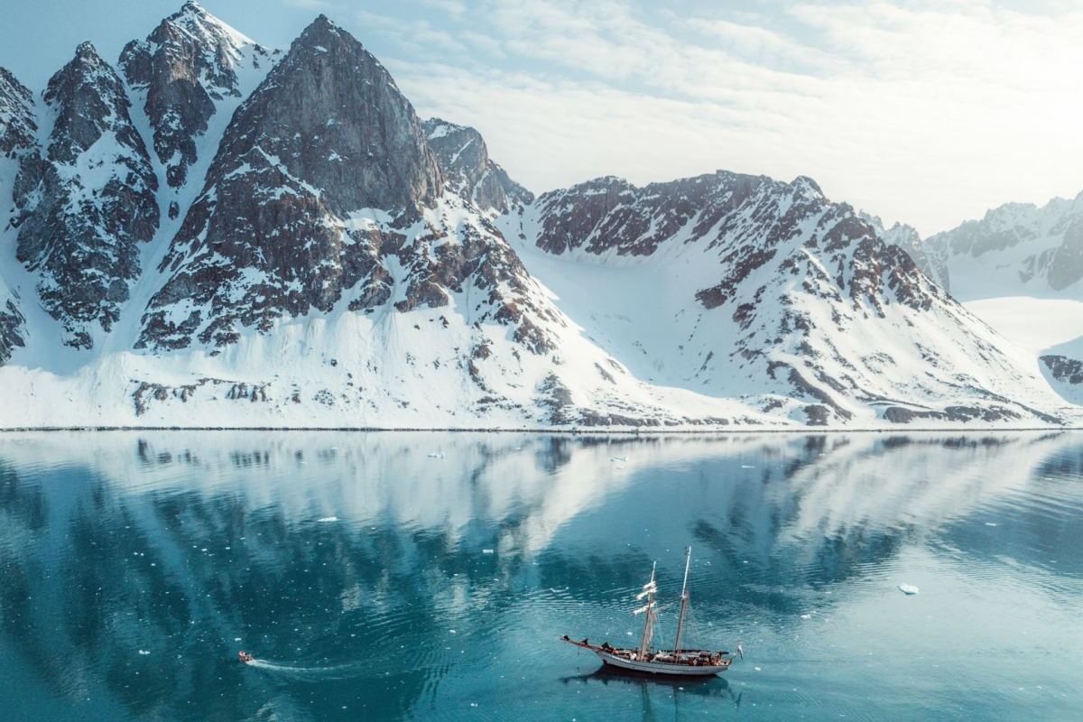Segelschiff Ocean Sherpa im Scoresbysund in Ostgrönland – Spiegelung der schneebedeckten Berge im türkisblauen Wasser unter klarem arktischem Licht.
