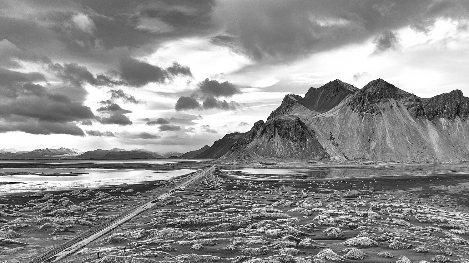 Stokksnes und Vestrahorn aus der Luft – Schwarz-Weiß-Aufnahme aus Island Schwarz-Weiß-Drohnenaufnahme von Stokksnes mit Vestrahorn, schwarzen Sanddünen und dramatischem Himmel in Island