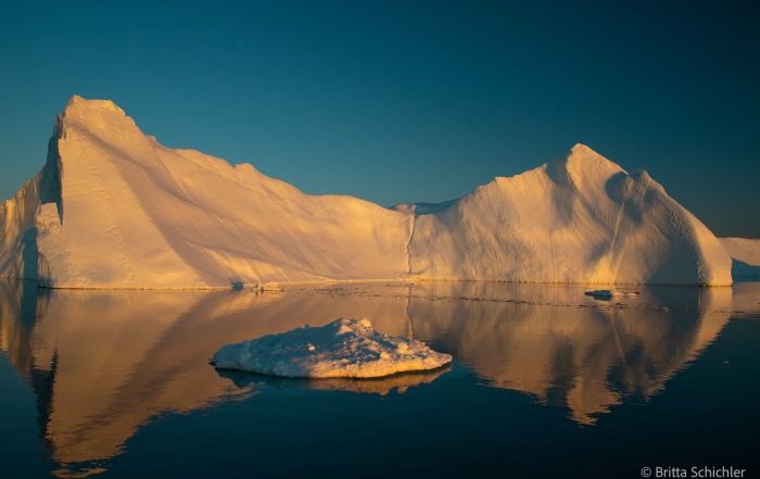 Großer Eisberg im warmen Abendlicht mit Spiegelung im Wasser der Diskobucht in Grönland