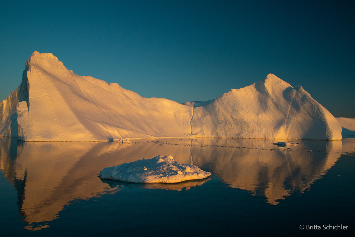 Großer Eisberg im warmen Abendlicht mit Spiegelung im Wasser der Diskobucht in Grönland