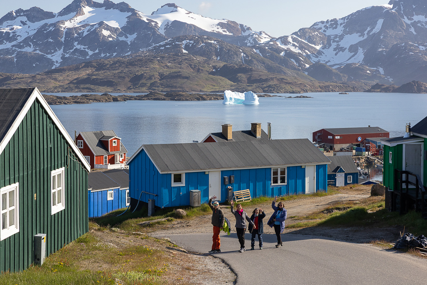 Vier Teilnehmerinnen einer Fotoreise zwischen bunten Häusern mit Eisberg und Bergen in Tasiilaq Ostgrönland