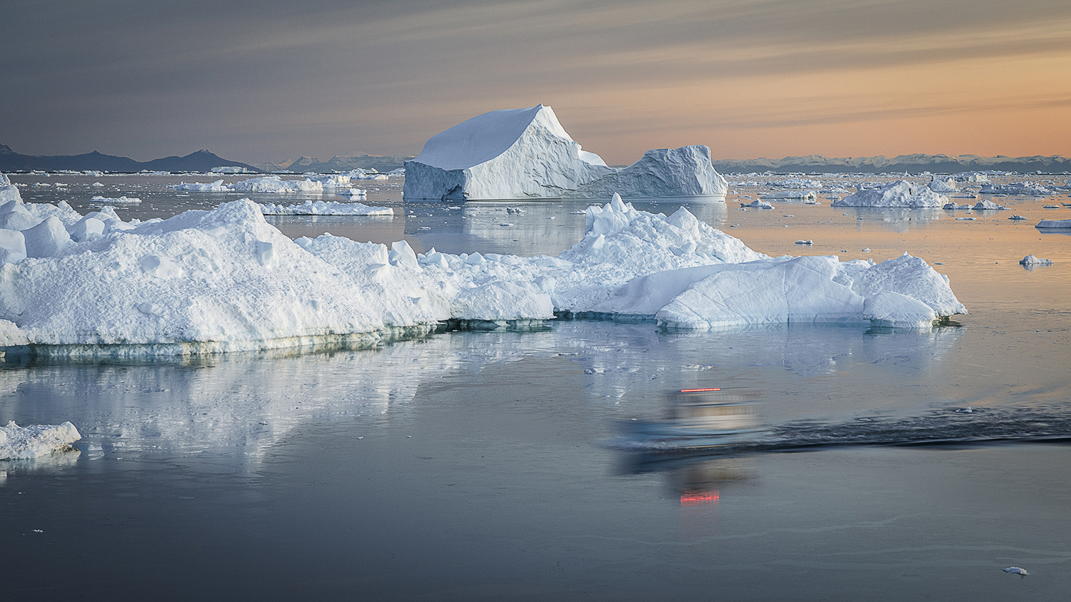 Eisberge in warmem Abendlicht in der Diskobucht bei Ilulissat, Grönland – ein Boot gleitet über das stille Wasser zwischen den Eismassen.