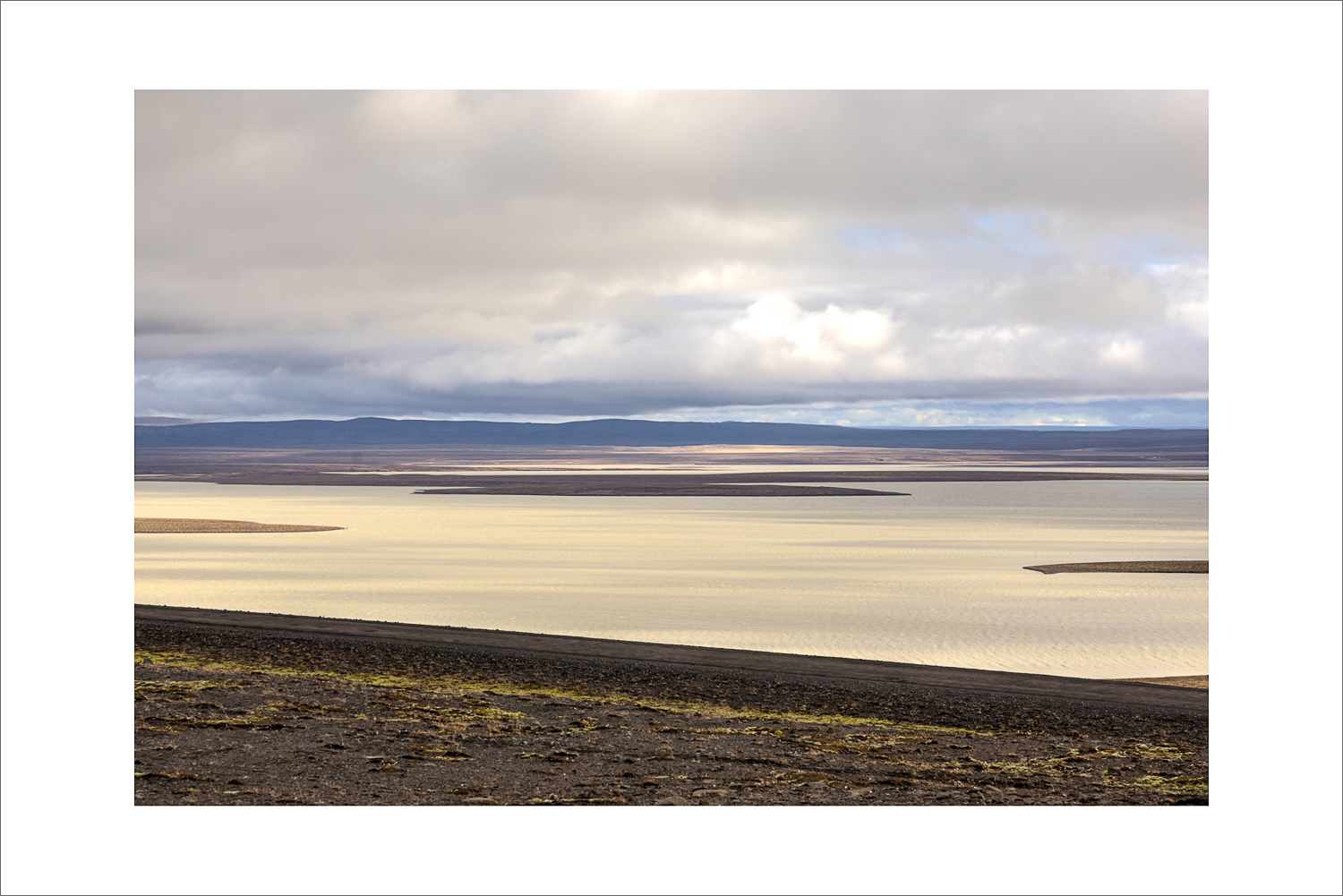 Panoramablick im zentralen Hochland Islands auf einen großen Stausee mit Inseln, karge Lavafläche im Vordergrund und dramatische Wolken über dem Wasser.