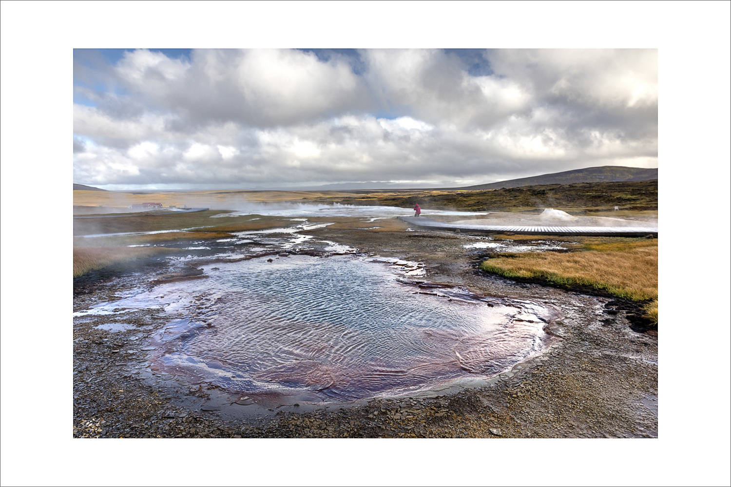 Geothermalgebiet Hveravellir im isländischen Hochland: dampfende heiße Quelle mit mineralischen Ablagerungen und Holzsteg, Wolkenhimmel über der Kjölur-Route (F35).
