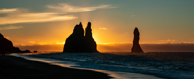 Sonnenaufgang hinter den Reynisdrangar-Felsen am schwarzen Strand von Reynisfjara, Island.
