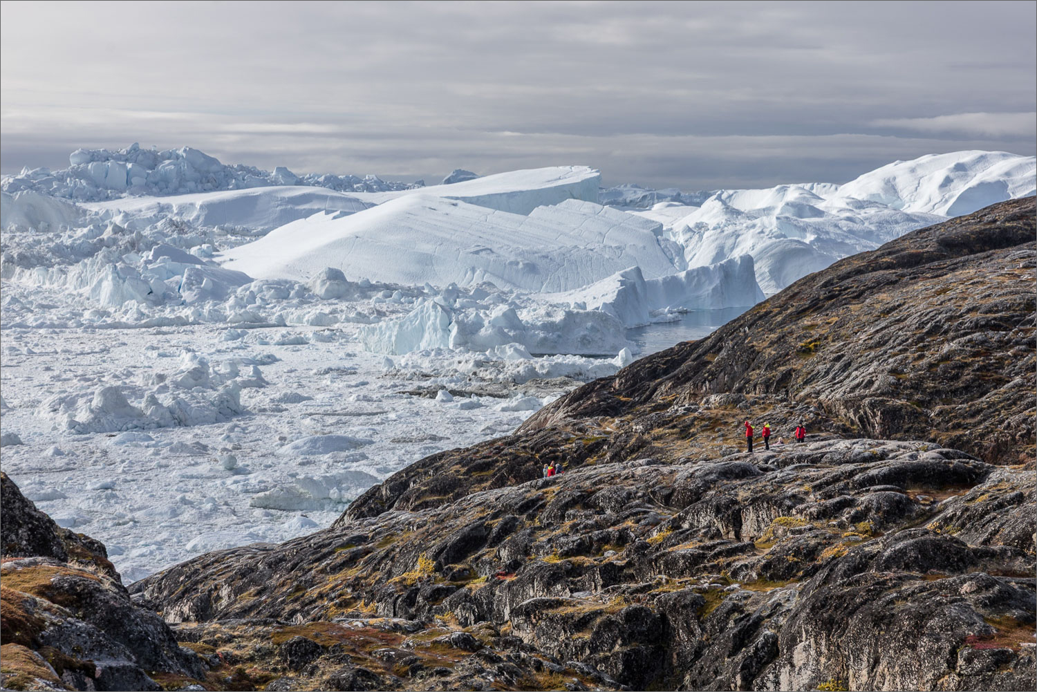 Menschen auf felsiger Anhöhe vor dem Eisfeld des Ilulissat Eisfjords während einer Fotoreise nach Grönland