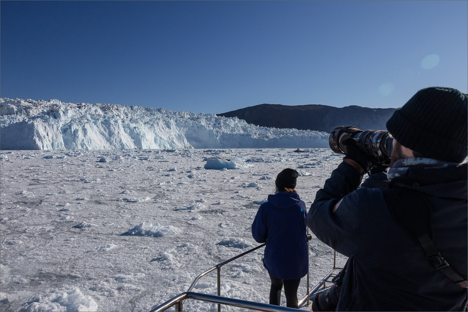 Fotografen auf einem Boot vor Anker vor dem Eqi-Gletscher in Westgrönland, Blick auf die kalbende Gletscherfront und Treibeis.