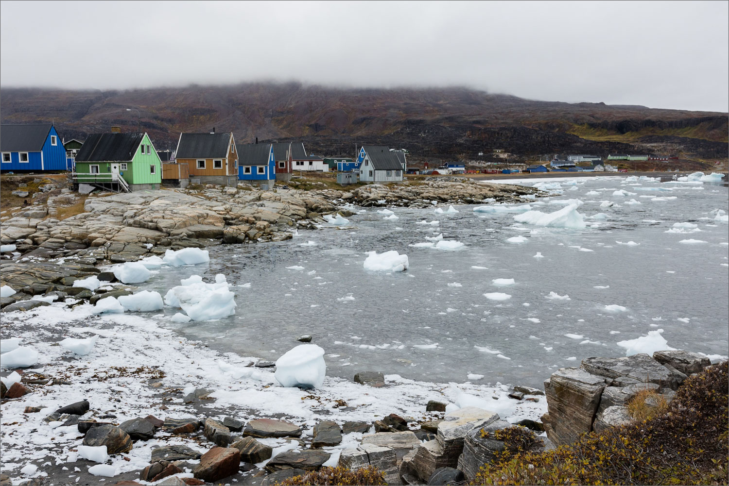 Küstenlandschaft von Qeqertarsuaq auf der Disko-Insel in Grönland mit bunten Häusern, treibendem Eis und arktischer Herbststimmung