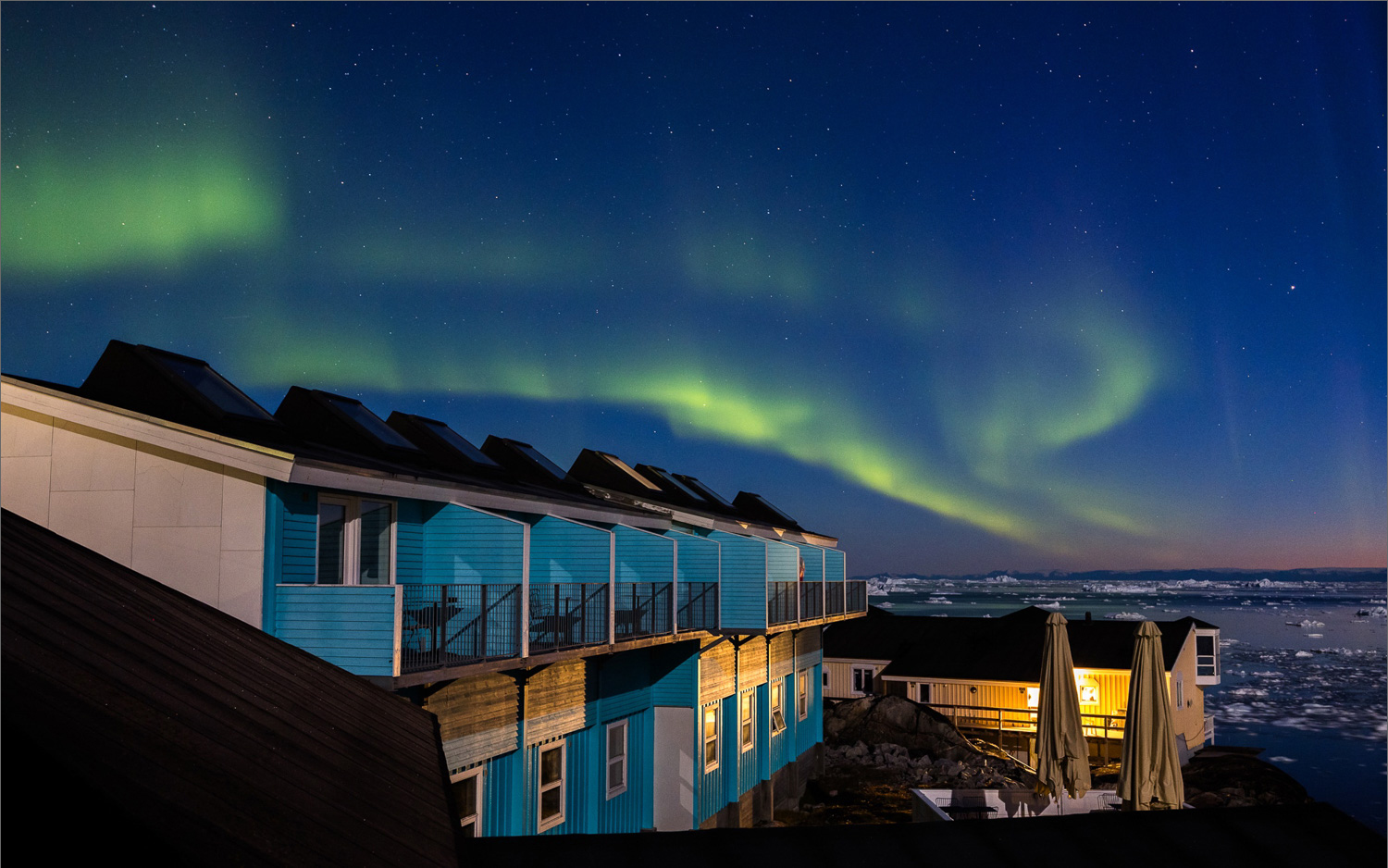 Polarlicht über der Diskobucht bei Ilulissat, Blick vom Balkon des Hotels Icefiord mit Nordlichtern, Sternenhimmel und Eisbergen im nächtlichen Westgrönland.