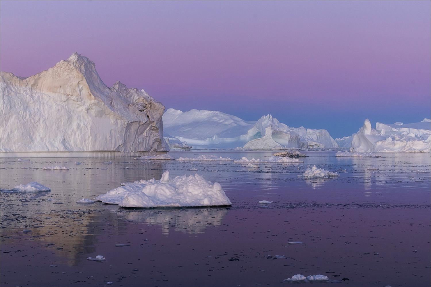 Eisberge in der Diskobucht bei Ilulissat im violetten Abendhimmel, ruhiges Wasser mit kleinen Eisschollen während der Blauen Stunde in Grönland.