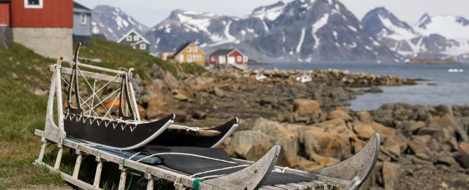 Traditionelle Hundeschlitten an der Küste von Kulusuk mit bunten Häusern und Bergen im Hintergrund