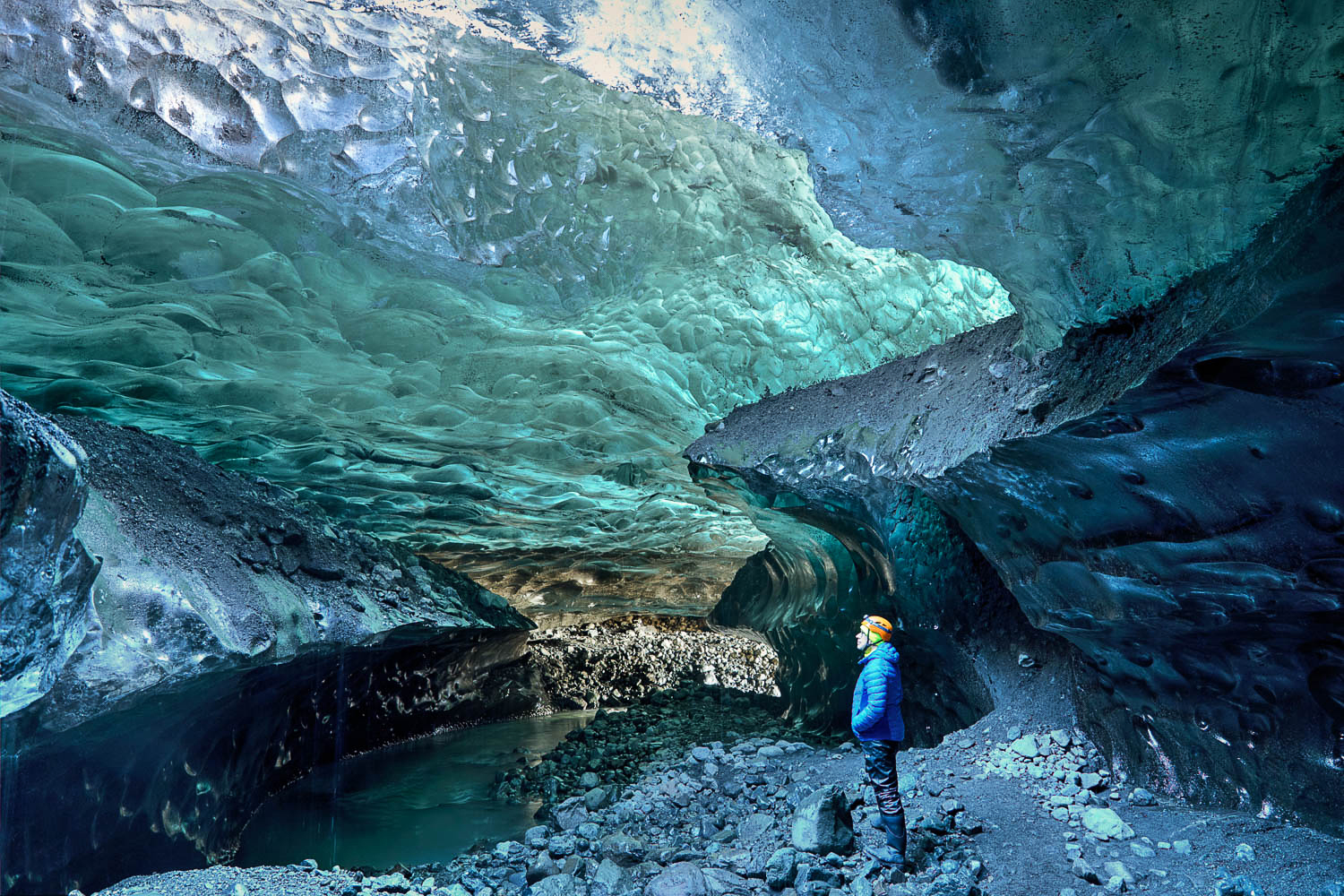 Island Eishöhle: Weite Kammer mit türkisblauem Eis Weite isländische Eishöhle mit türkisblauem Eis, Fels- und Eisformationen, eine Person steht im Vordergrund als Größenvergleich.