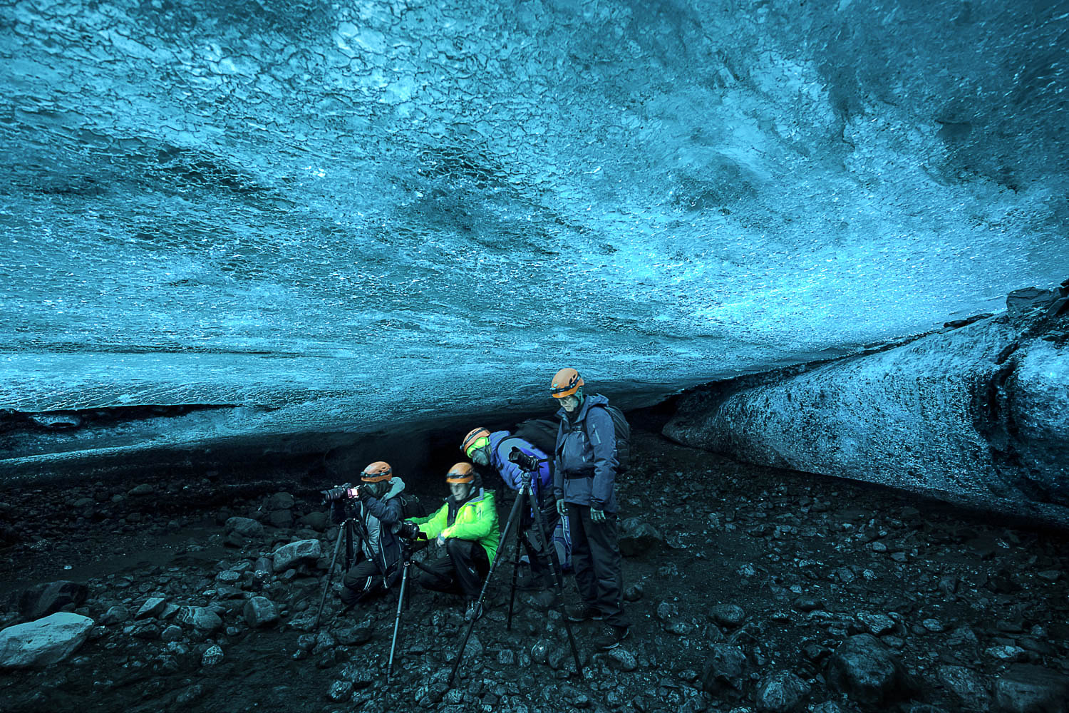 Island Gletscherhöhle: Fotografen unter blauem Eis Fotografen in einer isländischen Gletscherhöhle unter blau schimmerndem Eis, Stirnlampen leuchten, dunkler Boden mit Steinen.