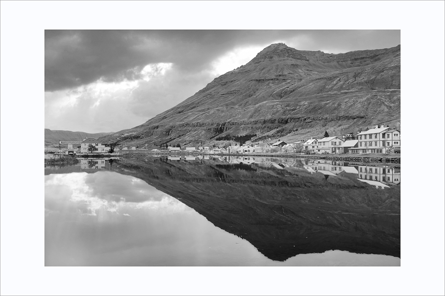 Schwarzweißaufnahme von Seyðisfjörður mit Spiegelung im Wasser in den Ostfjorden Islands