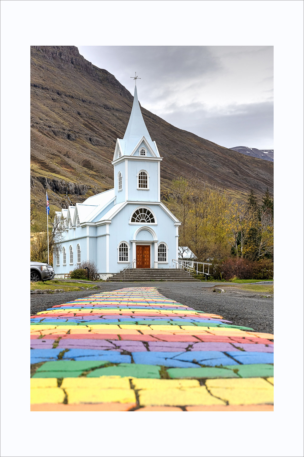 Hellblaue Kirche von Seyðisfjörður mit Regenbogenweg in den Ostfjorden Islands