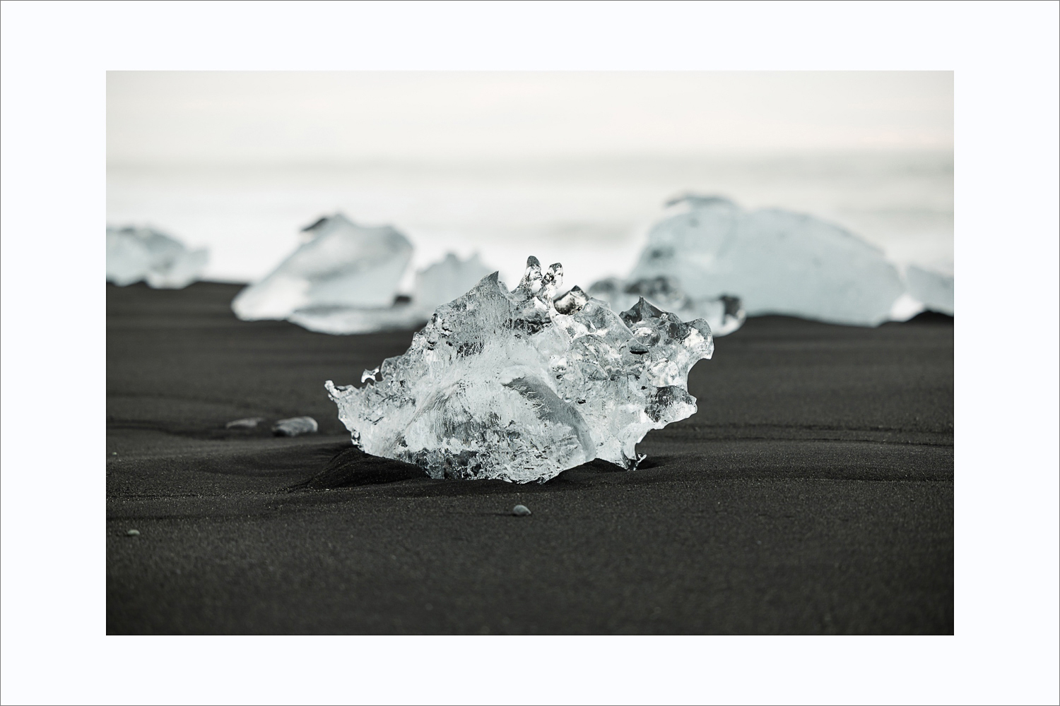Eisdetail am Diamond Beach in Island auf schwarzem Sand mit unscharfen Eisblöcken im Hintergrund