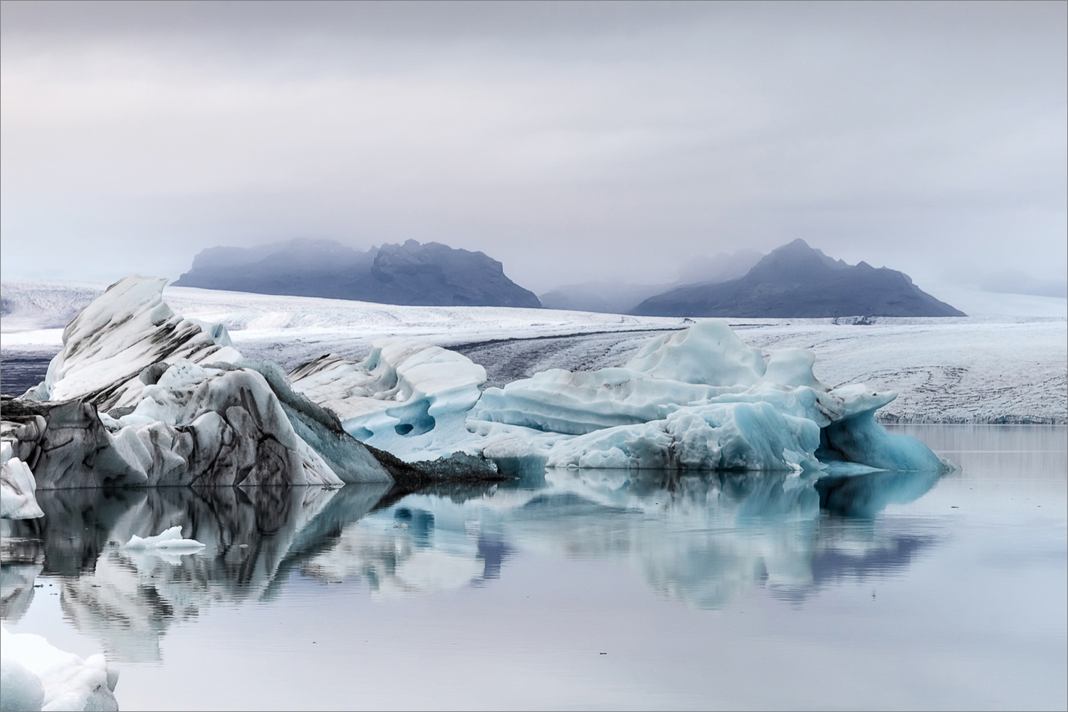Eisberge in der Gletscherlagune Jökulsárlón in Island mit Spiegelung und Gletscher im Hintergrund