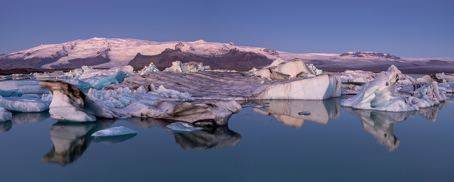 Jökulsárlón in der blauen Stunde: Eisberge im ruhigen Wasser Panorama der Gletscherlagune Jökulsárlón in Island in der blauen Stunde mit treibenden Eisbergen, ruhigem Wasser und Gletscherbergen im Hintergrund.