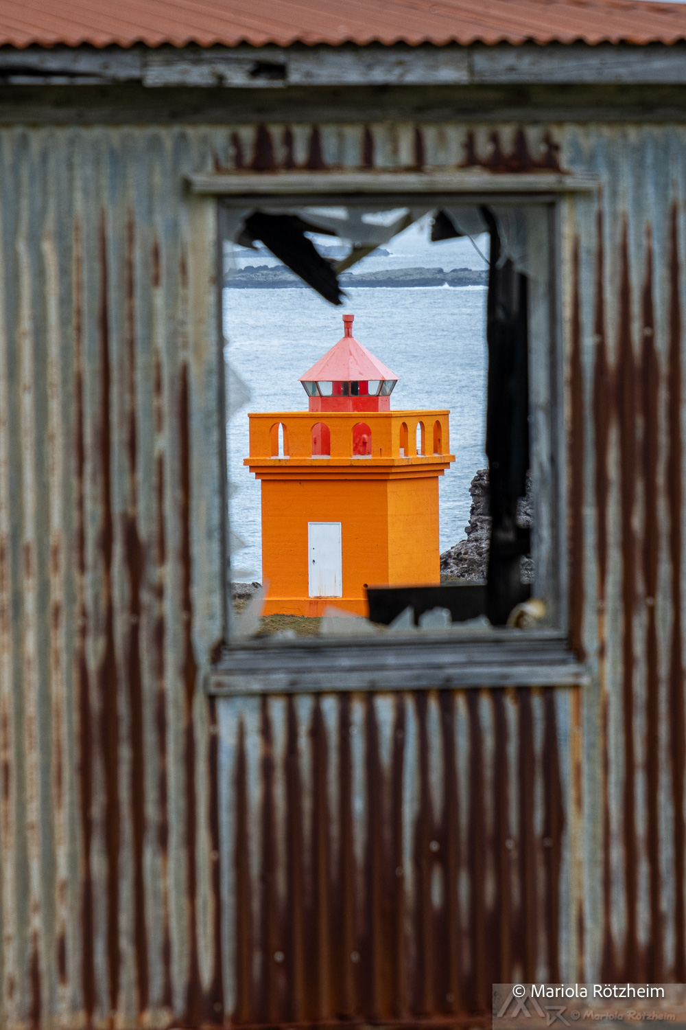 Oranger Leuchtturm in Djúpivogur durch ein zerbrochenes Fenster fotografiert