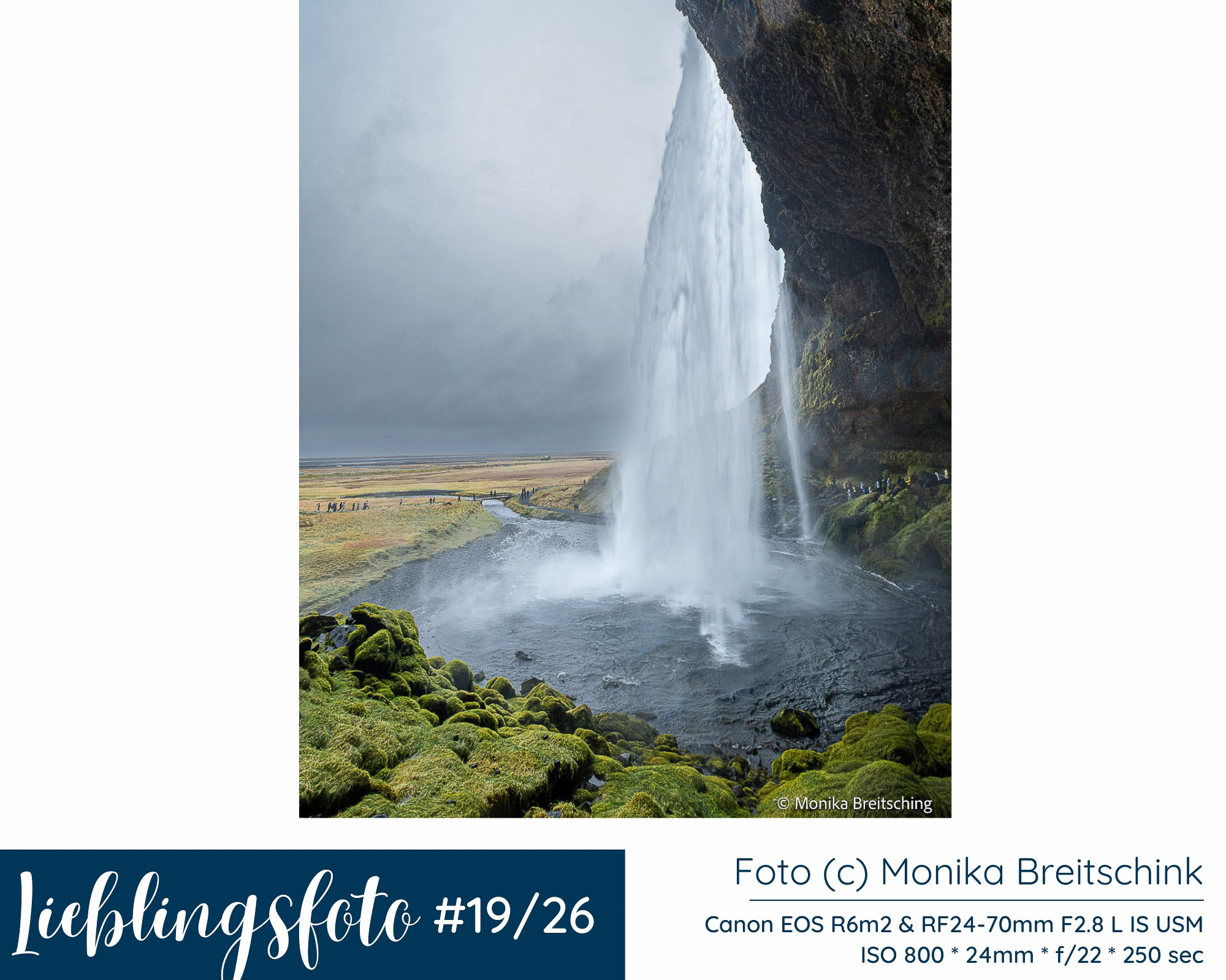 Blick hinter den Seljalandsfoss in Südisland mit fallendem Wasser, Felswand, grünem Moos und Landschaft im Hintergrund
