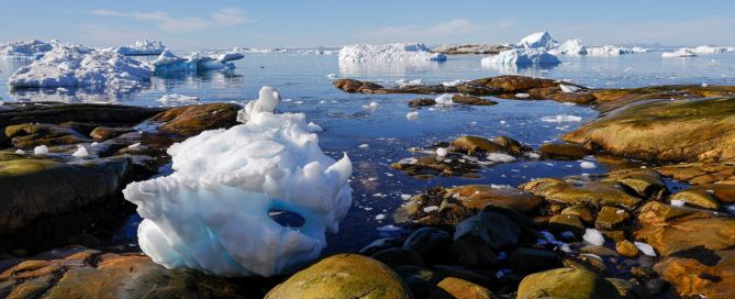 Eisberge in der Diskobucht bei Ilulissat in Westgrönland mit Felsen, ruhigem Wasser und klarem blauem Himmel