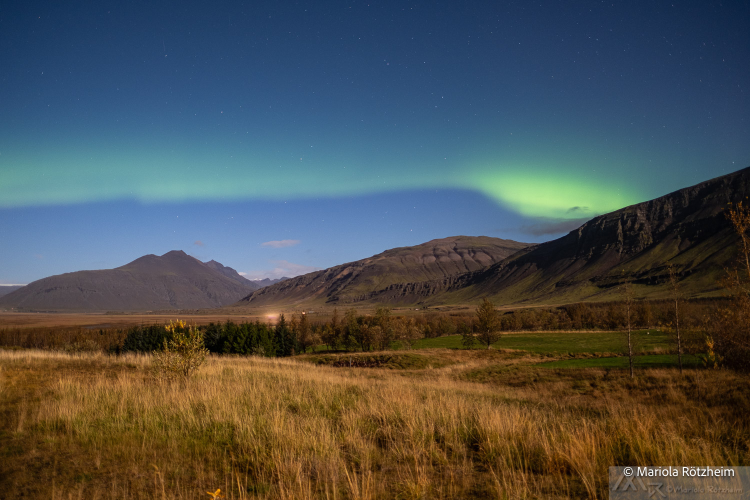 Schwaches Polarlicht über der Landschaft in Südisland Zartes grünes Polarlicht über Bergen und Wiesen im Süden Islands