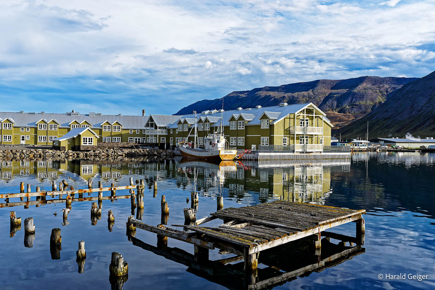 Holzsteg und Spiegelungen im Hafen von Siglufjörður vor den Bergen Nordislands