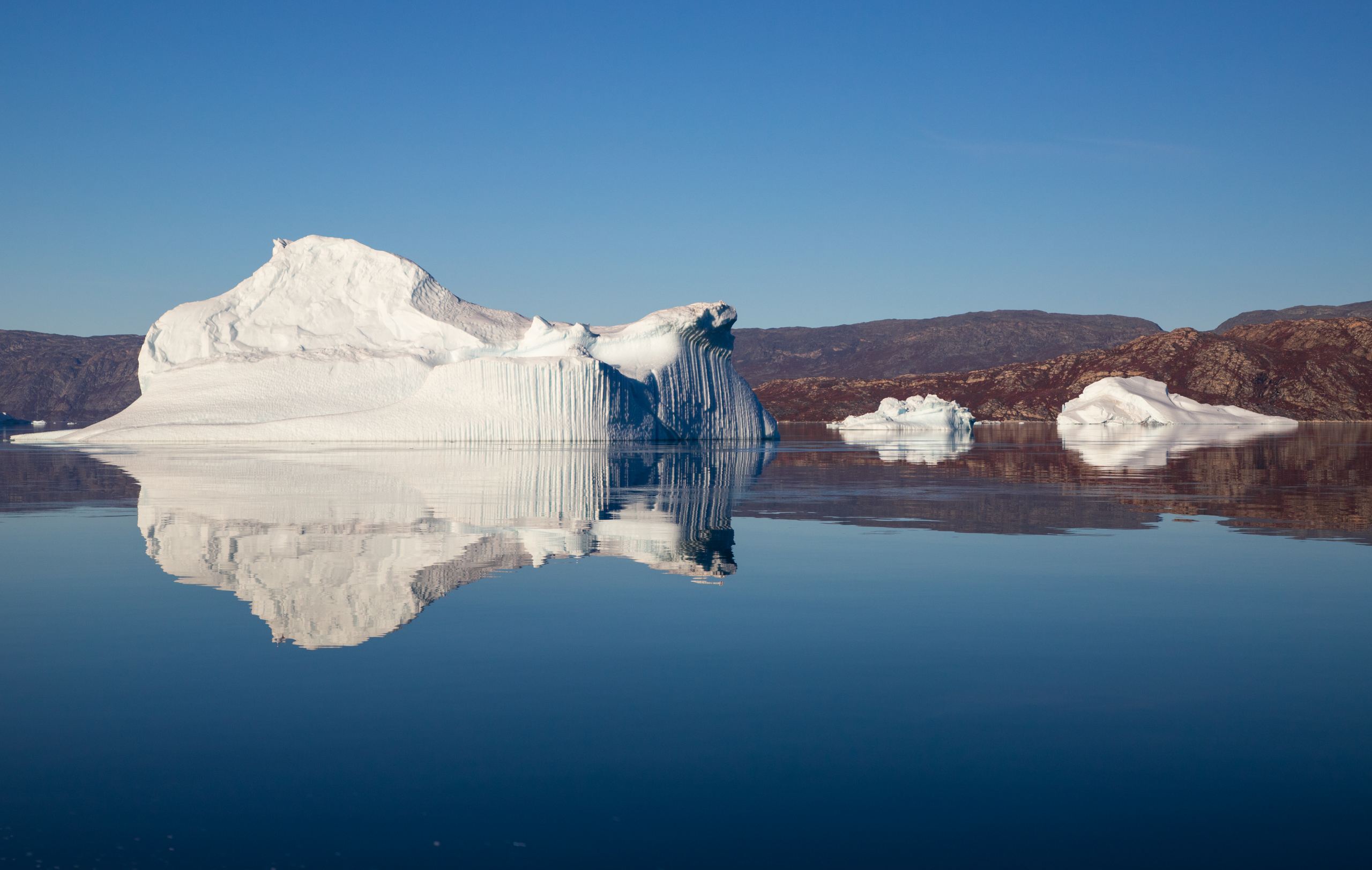 Großer weißer Eisberg mit nahezu symmetrischer Spiegelung im ruhigen Wasser in Westgrönland