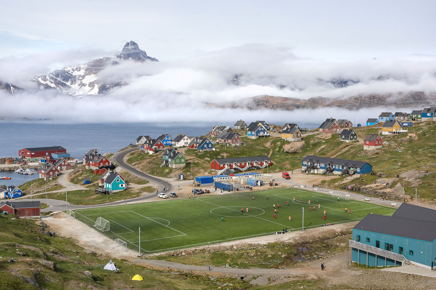 Tasiilaq in Ostgrönland Blick über Tasiilaq mit bunten Häusern, Fußballplatz und wolkenverhangenen Bergen in Ostgrönland Foto: Radmila Dier