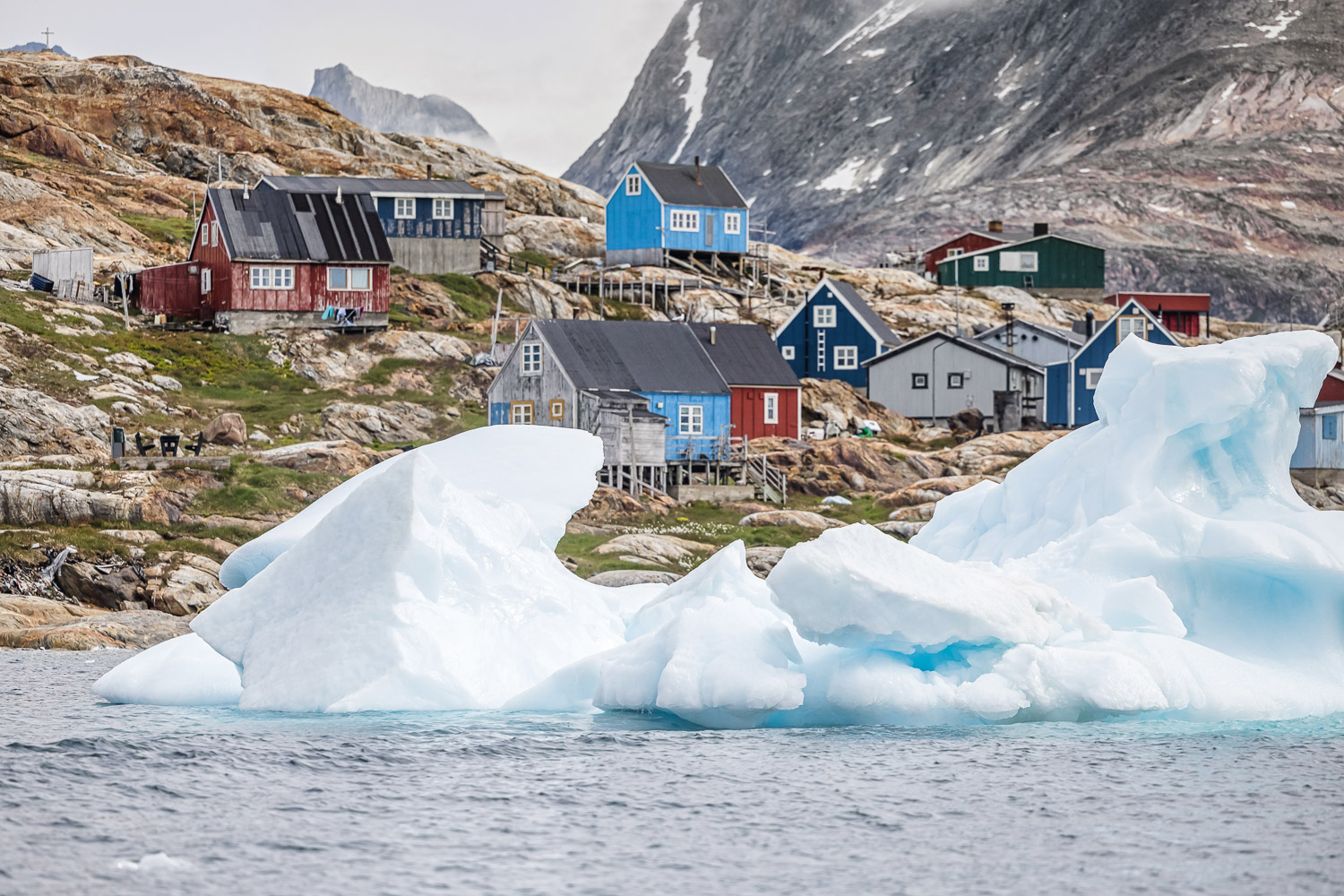 Tiniteqilaaq in Ostgrönland Bunte Häuser von Tiniteqilaaq hinter einem großen Eisberg in Ostgrönland